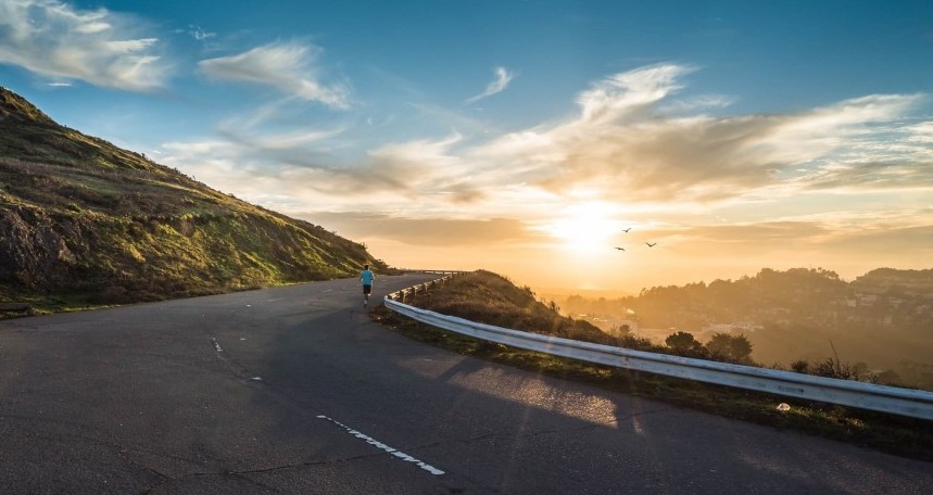 Man running up a road as the sun sets over the ocean